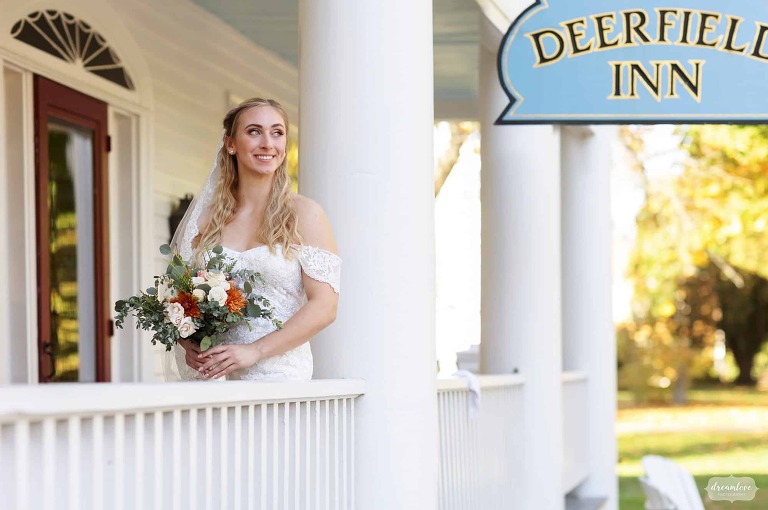 Bride looks out from white porch at Deerfield Inn in MA.