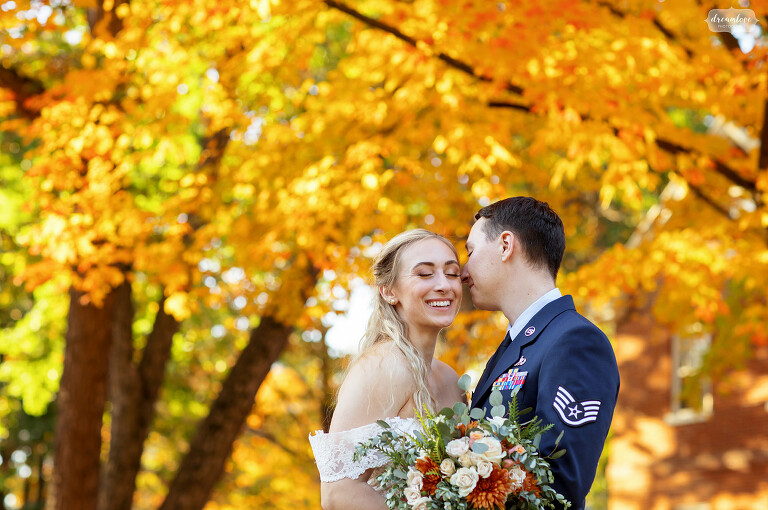 Happy smiling bride with groom in front of bright orange fall foliage in MA.